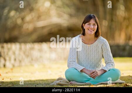 Portrait d'une jeune femme souriante se reposant sur une couverture dans un parc ensoleillé Banque D'Images