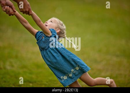 Bonne petite fille qui s'amuse quand son père la balance sur la pelouse Banque D'Images