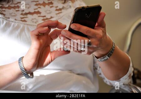 Femme caucasienne tenant un smartphone envoyant un message à l'extérieur. Porter une chemise blanche. Montre et anneaux argentés, gens modernes, nouveau millénaire Banque D'Images