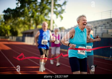 Une femme senior heureuse franchit la ligne d'arrivée en premier dans une course à pied. Banque D'Images