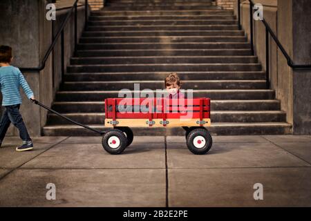 Jeune garçon dans un wagon tiré le long d'un trottoir par son frère aîné Banque D'Images