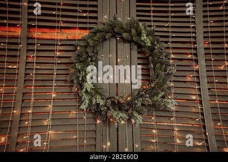 Magnifique couronne d'arbre de Noël accrochée sur un mur de bois et de brique avec de nombreuses ampoules et guirlandes suspendues Banque D'Images