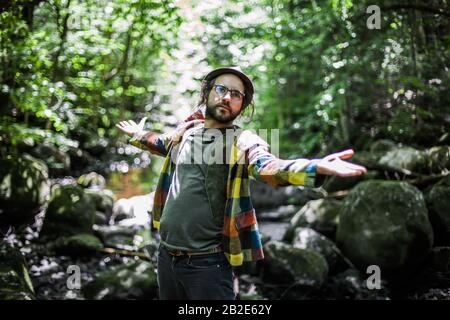 Un jeune homme caucasien a largement ouvert ses bras et accueillant tout le monde pour commencer à faire du trekking dans la forêt. Un homme barbu qui s'amuse à la nature. Banque D'Images