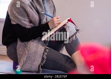 Femme imreconnaissable étudiant le yoga. Une femme prend des notes. Prise de vue moyenne. Une femme âgée a écrit des notes pendant l'atelier dans le centre de yoga Banque D'Images