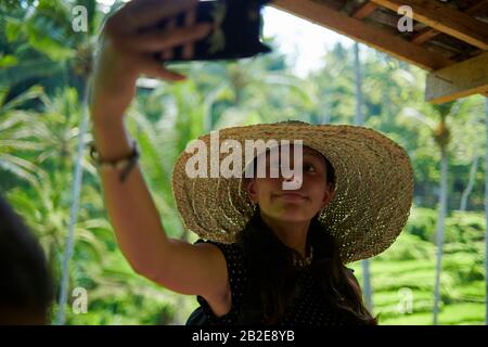 Jeune fille portant un gros chapeau de paille prenant des selfies en utilisant le téléphone mobile Banque D'Images