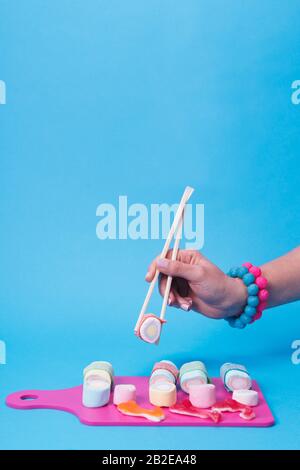 Main féminine utilisant des baguettes avec des sushis en sucre Banque D'Images
