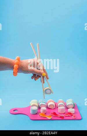 Main féminine utilisant des baguettes avec des sushis en sucre Banque D'Images