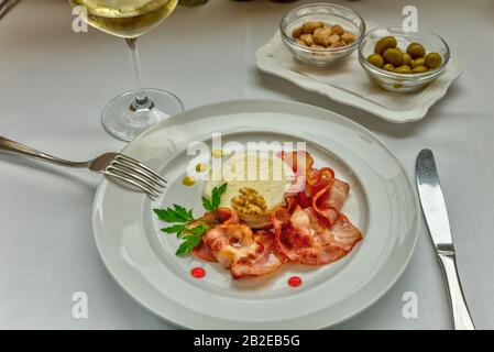 Fromage de chèvre chaud au miel et au bacon servi sur un plat blanc, servi avec un verre de vin blanc délicat. Banque D'Images