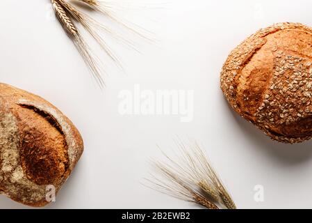 Composition à plat avec deux pains de délicieux pain rustique et des oreilles de blé isolés sur un fond blanc avec de l'espace pour le texte. Affaires de boulangerie c Banque D'Images