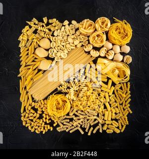 Assortiment de pâtes italiennes, une couche carrée plate de nombreux types de pâtes différents, tiré d'en haut sur un fond noir Banque D'Images