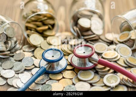 Gros plan bleu stéthoscope et pot de pièce de monnaie sur table en bois. Concept de contrôle financier et financier Banque D'Images