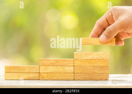 Gros plan tenant les mains bloque le bois pour faire monter le pas sur fond de flou vert avec l'espace de copie pour le texte ou le concept de conception pour le concept d'affaires Banque D'Images