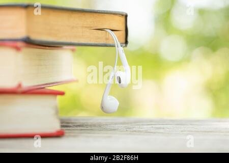 Gros plan livre et écouteurs blancs sur table en bois avec fond de flou vert abstrait. Concept de lecture et d'éducation Banque D'Images