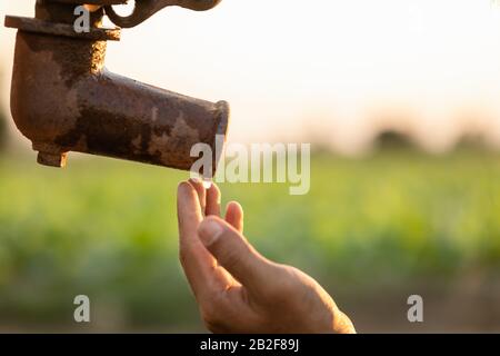 Gros plan main de fermier attendant l'eau de la pompe à eau extérieure vintage. Pour le concept de saison de sécheresse Banque D'Images