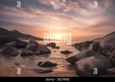 Le soleil se situe sur la côte rocheuse et la plage de sable près du village d'Algajola dans la région de Balagne en Corse Banque D'Images