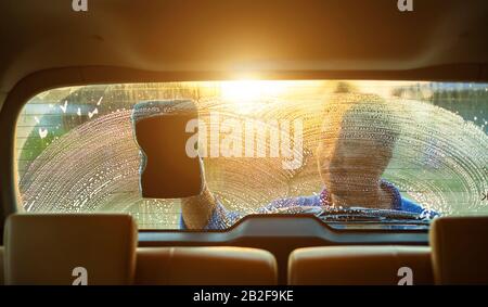 Homme asiatique utilisant une éponge bleue avec du savon pour laver la voiture à l'extérieur au coucher du soleil. Concept de nettoyage et d'entretien de voiture Banque D'Images