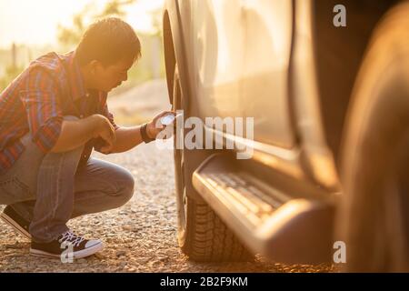 Homme asiatique qui contrôle la pression d'air et remplit l'air dans les pneus de sa voiture. Entretien de la voiture avant la conduite concept Banque D'Images