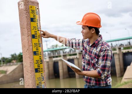 Jeune ingénieur asiatique travaillant sur place au barrage et vérifiant le niveau de jauge sur le poteau Banque D'Images