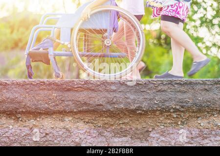 Les personnes poussant le fauteuil roulant et marchant près de la cause endommagée de la route de la forte pluie et de la terre glissante. Concentrez-vous sur la texture de la route Banque D'Images