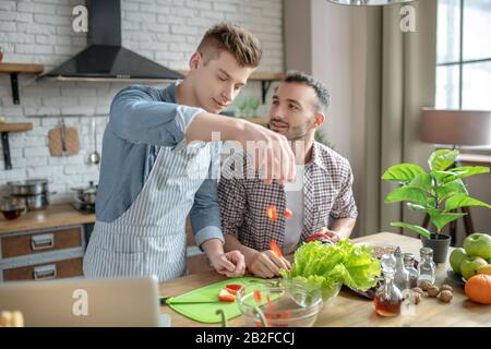 De jeunes hommes cuisant de la salade de légumes dans la cuisine. Banque D'Images