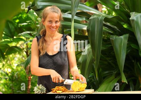 une jeune fille à trancher d'ananas mûrs et frais se trouve sur une table en bois dans un jardin tropical du sri lanka Banque D'Images