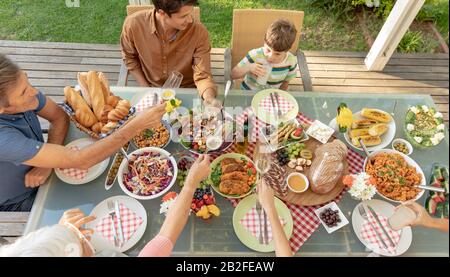 Vue en grand angle d'une famille caucasienne de plusieurs générations avec lunettes et pain grillé assis à l'extérieur à une table de dîner pour un repas. Famille enj Banque D'Images