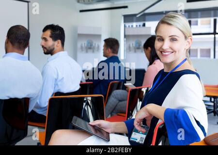 Vue latérale d'une femme d'affaires caucasienne travaillant dans un foyer moderne, assis et se tournant, regardant l'appareil photo et souriant, tenant un numérique Banque D'Images