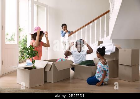 Vue de face d'un couple afro-américain avec son fils et sa fille à la maison, en essayant des chapeaux et en déballant des boîtes dans un couloir. Famille profitant du temps à h Banque D'Images