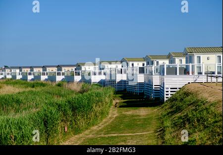 Chemin herbacé incurvé devant la rangée de caravanes statiques blanches identiques avec patios, West Sands Caravan Park, Bunn Leisure, Selsey, West Sussex, Angleterre Banque D'Images