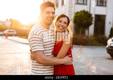 Image d'un couple caucasien joyeux en vêtements d'été riant et embrassant tout en marchant dans la rue de la ville Banque D'Images