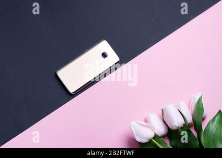 Carte de vœux avec téléphone mobile et tulipes roses printanières fleur sur fond de diagonale duotone. Banque D'Images