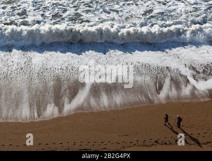 Vieux couple marchant sur la plage de sable avec des vagues blanches, vue aérienne, Dorset, Angleterre, Royaume-Uni