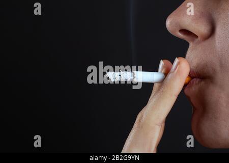 la femme fume une cigarette sur fond sombre. dépendance à la nicotine. fumée de tabac. Banque D'Images