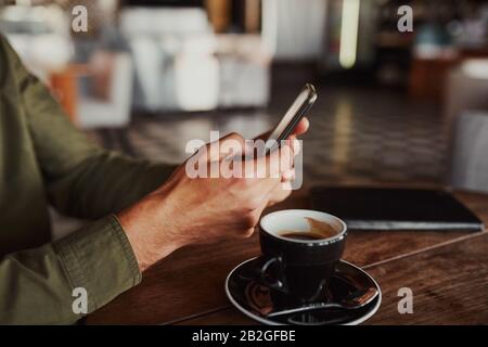 Gros plan sur les mains de l'homme à l'aide d'un smartphone tout en étant assis dans un café en buvant du café Banque D'Images