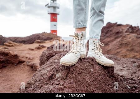 Voyageur debout sur la terre rocheuse, voyageant des terres volcaniques près du phare. Vue sur les chaussures de randonnée de la femme Banque D'Images