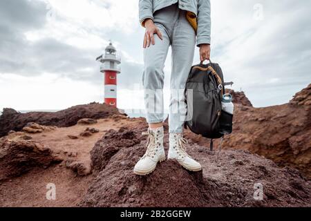 Voyageur avec sac à dos debout sur la terre rocheuse, voyage volcanique landsacpes près du phare. Vue sur les chaussures de randonnée de la femme Banque D'Images