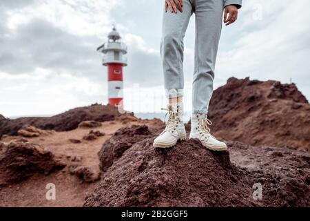 Voyageur debout sur la terre rocheuse, voyageant des terres volcaniques près du phare. Vue sur les chaussures de randonnée de la femme Banque D'Images