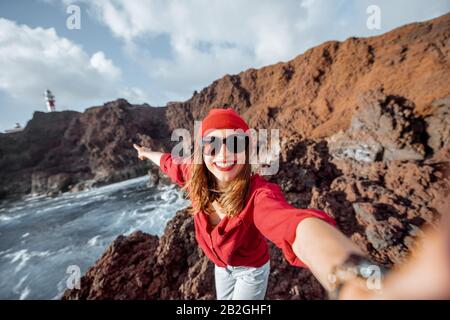 Jeune femme élégante faisant des portraits de selfie tout en voyageant sur la côte rocheuse de l'océan près du phare sur l'île de Tenerife, Espagne Banque D'Images