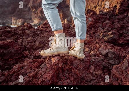 Voyageur debout sur la terre rocheuse, voyageant des terres volcaniques près du phare. Vue sur les chaussures de randonnée de la femme Banque D'Images