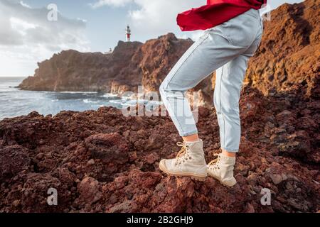 Voyageur debout sur la terre rocheuse, voyageant des terres volcaniques près du phare. Vue sur les chaussures de randonnée de la femme Banque D'Images