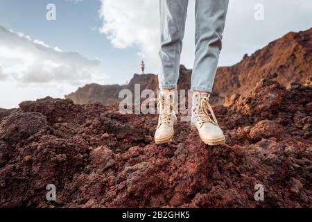 Voyageur debout sur la terre rocheuse, voyageant des terres volcaniques près du phare. Vue sur les chaussures de randonnée de la femme Banque D'Images