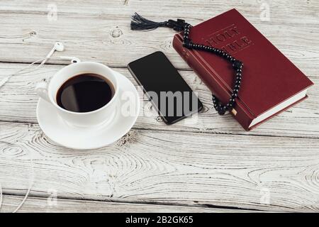 Bible Sainte et smartphone avec tasse de café noire sur fond en bois. Banque D'Images