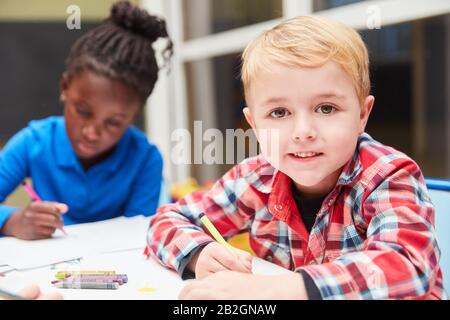 Un garçon blond peint sur du papier à la maternelle avec de la rayonne à la table Banque D'Images