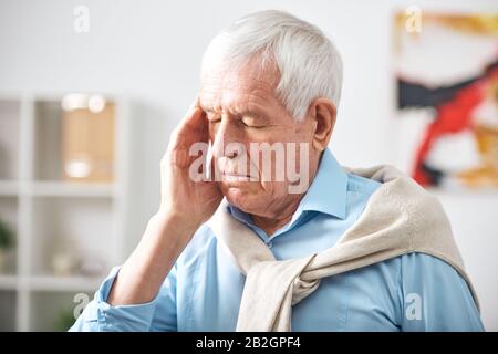 Homme épuisé à poil blanc avec des yeux fermés touchant le temple tout en se sentant mal à la tête Banque D'Images