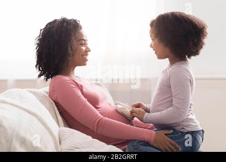 Petite fille mettant de petites chaussures de bébé sur le ventre enceinte de maman Banque D'Images