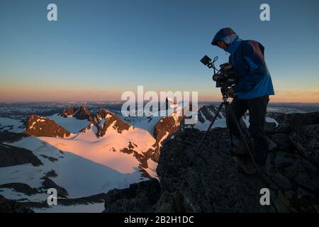 Homme filmant sur le dessus du monde, sur le sommet, regardant dans les montagnes Banque D'Images