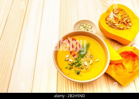 Soupe maison à la crème de citrouille chaude d'automne avec bacon frappé et graines. Citrouille brute, ciboulette fraîche, aneth, sel dans la cuillère sur fond de bois Banque D'Images