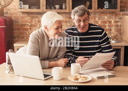 Couple Senior Souriant Lecture Du Contrat De Police D'Assurance Maladie Dans La Cuisine Ensemble Banque D'Images