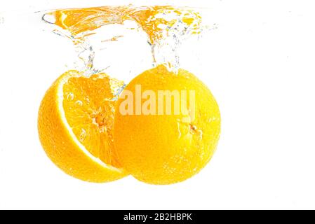 Orange organique tranché en deux temps s'enfonçant dans de l'eau cristalline avec des bulles d'air Banque D'Images