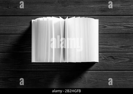 Un livre blanc avec des pages blanches se trouve sur un fond en bois noir Banque D'Images